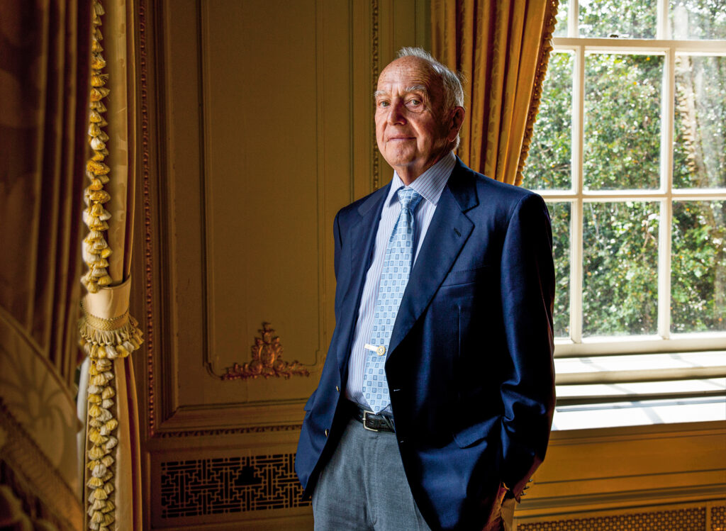 A man stands by a set of windows wearing a suit and tie.