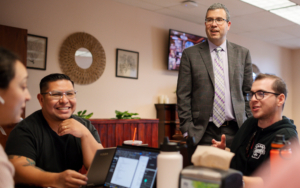 A man in suit stands chatting with students who are studying for finals.
