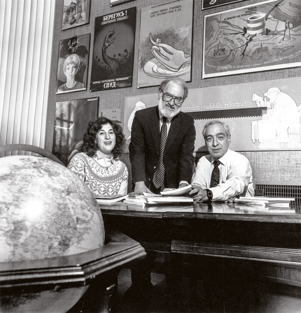 Three people sit at a table reviewing books in black and white.