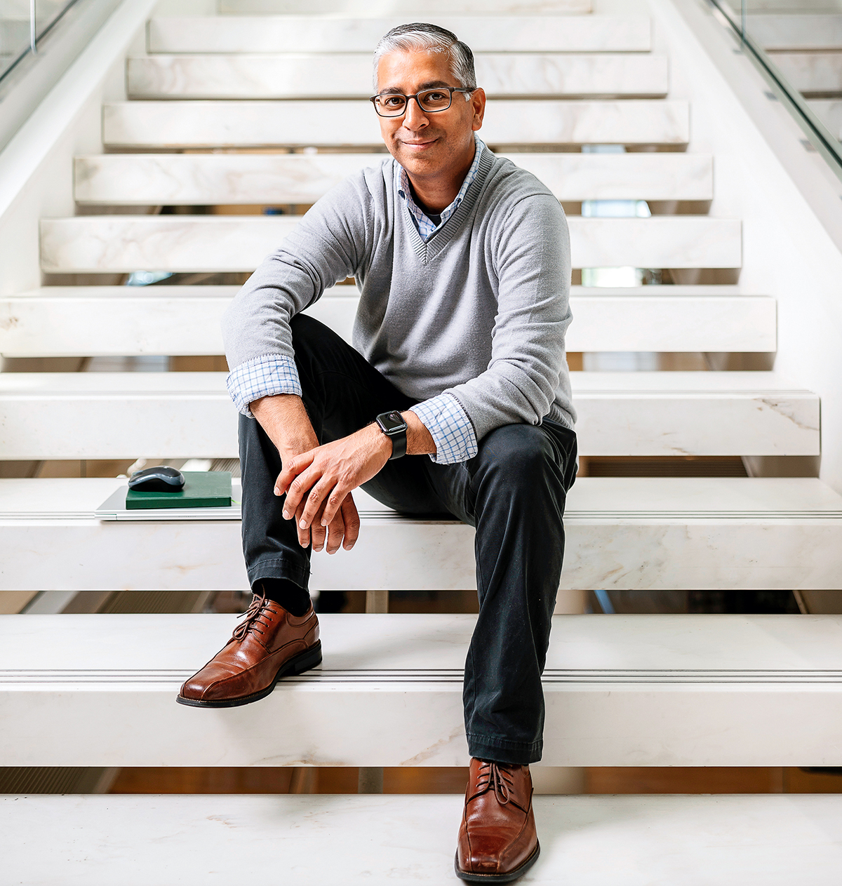 A man wearing glasses sits on a staircase.