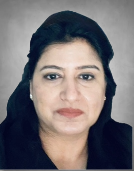 A professional headshot of a woman wearing dark clothing. She has dark hair and is photographed against a neutral gray background with a composed, professional expression.
