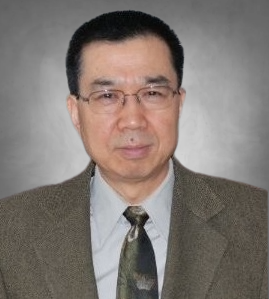 A professional headshot of a man with short black hair wearing rectangular glasses. He is dressed in a brown textured blazer, a light collared shirt, and a dark patterned tie. He is looking at the camera against a neutral gray background.