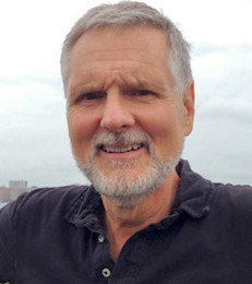 Headshot of Robert McGrath, smiling while wearing a dark polo shirt outdoors with buildings in the background.