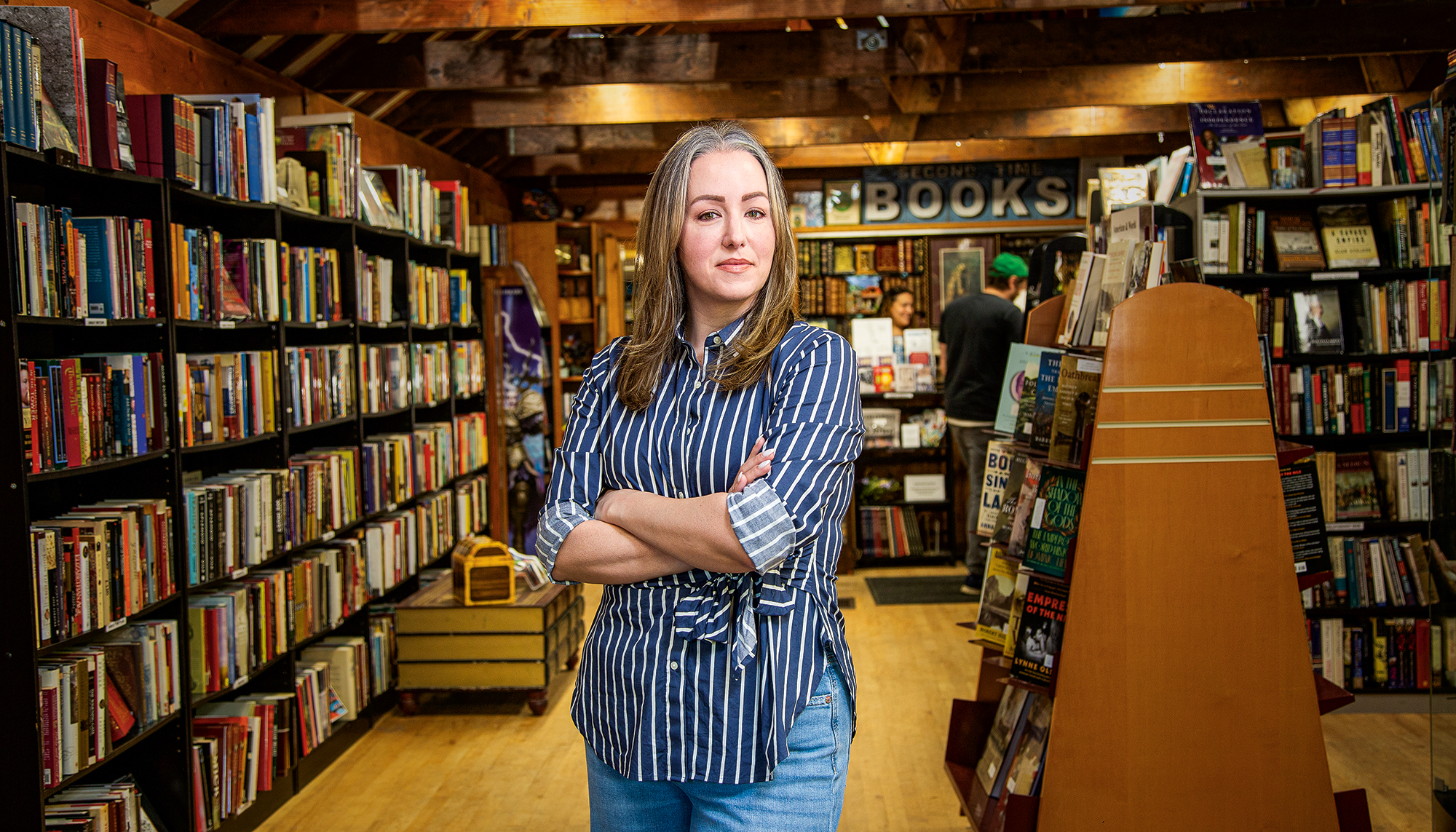 A woman stands with her arms crossed in a bookstore.