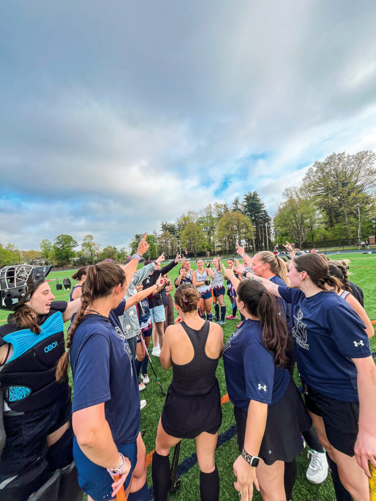 A group of field hockey players stand on the field after an alumni game.