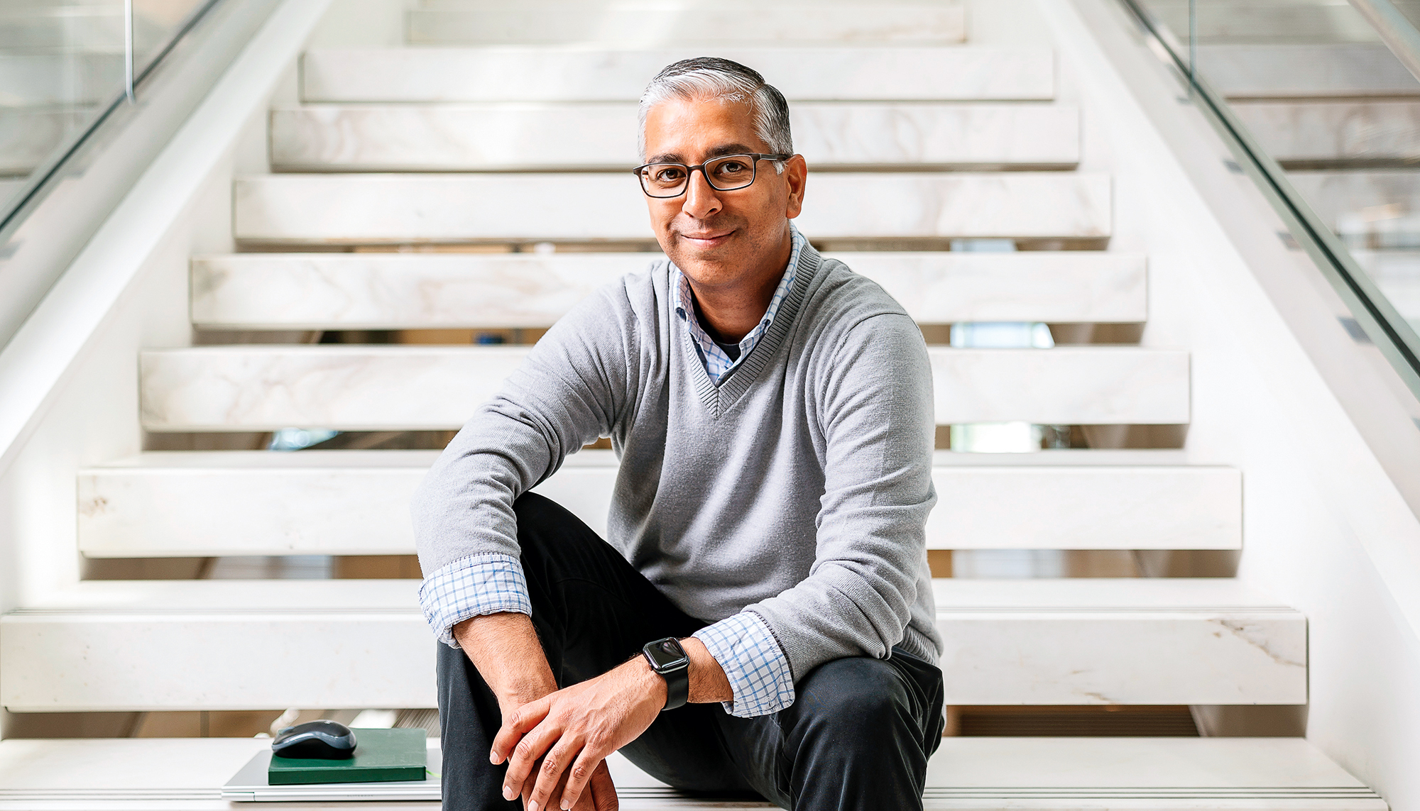A man wearing glasses sits on a staircase.