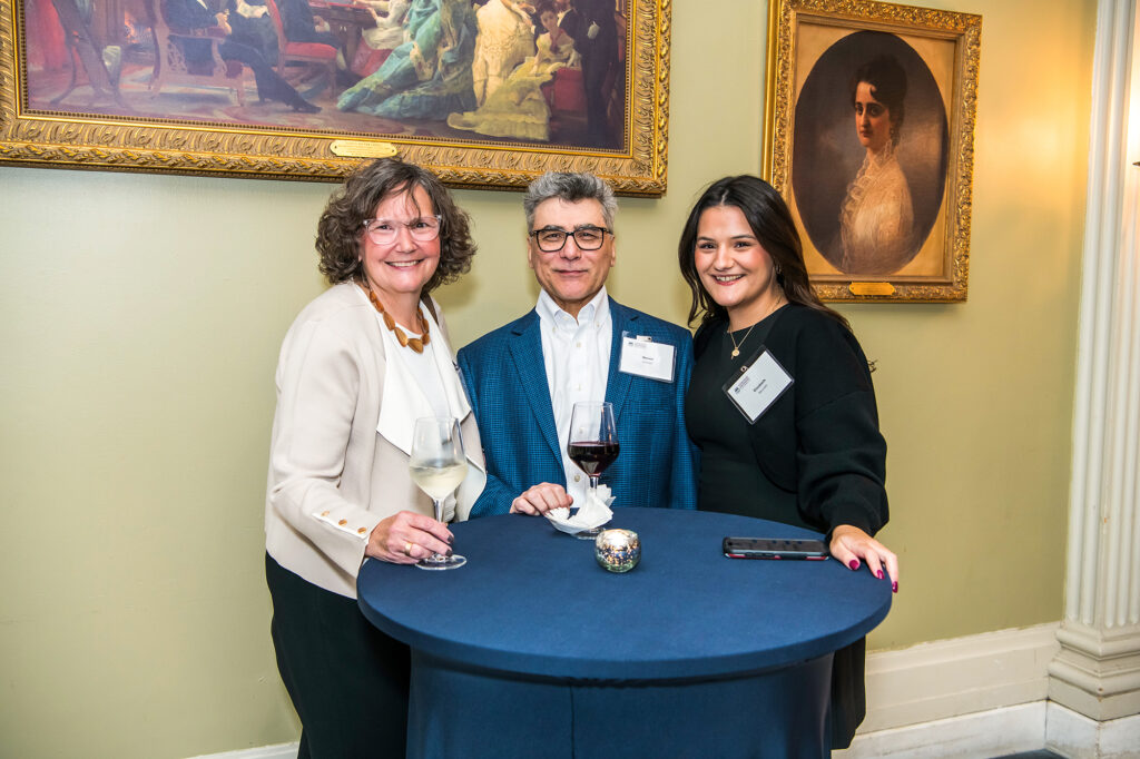 Two women and one man stand together at a table with a navy blue table cloth.