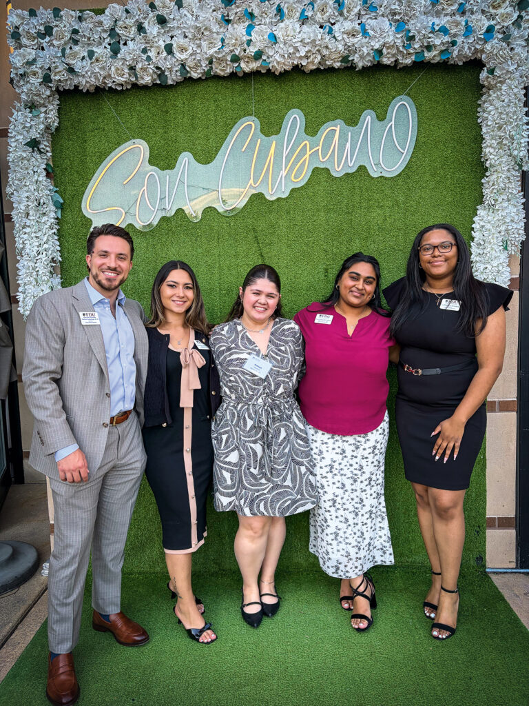 Four women and one man stand together against a bright green backdrop.