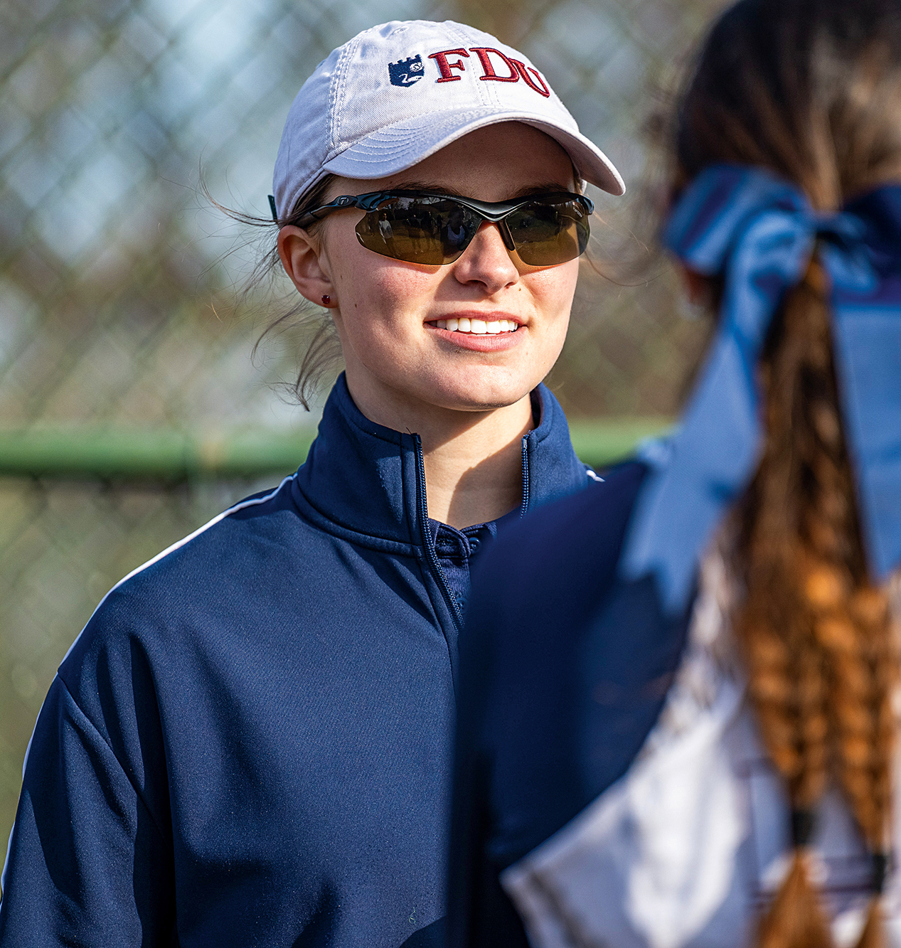 A woman wears sunglasses and an FDU baseball hat.