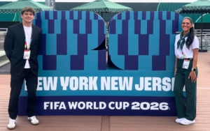 two FDU college students pose with a sign for the FIFA World Cup 2026. they are dressed in professional attire.