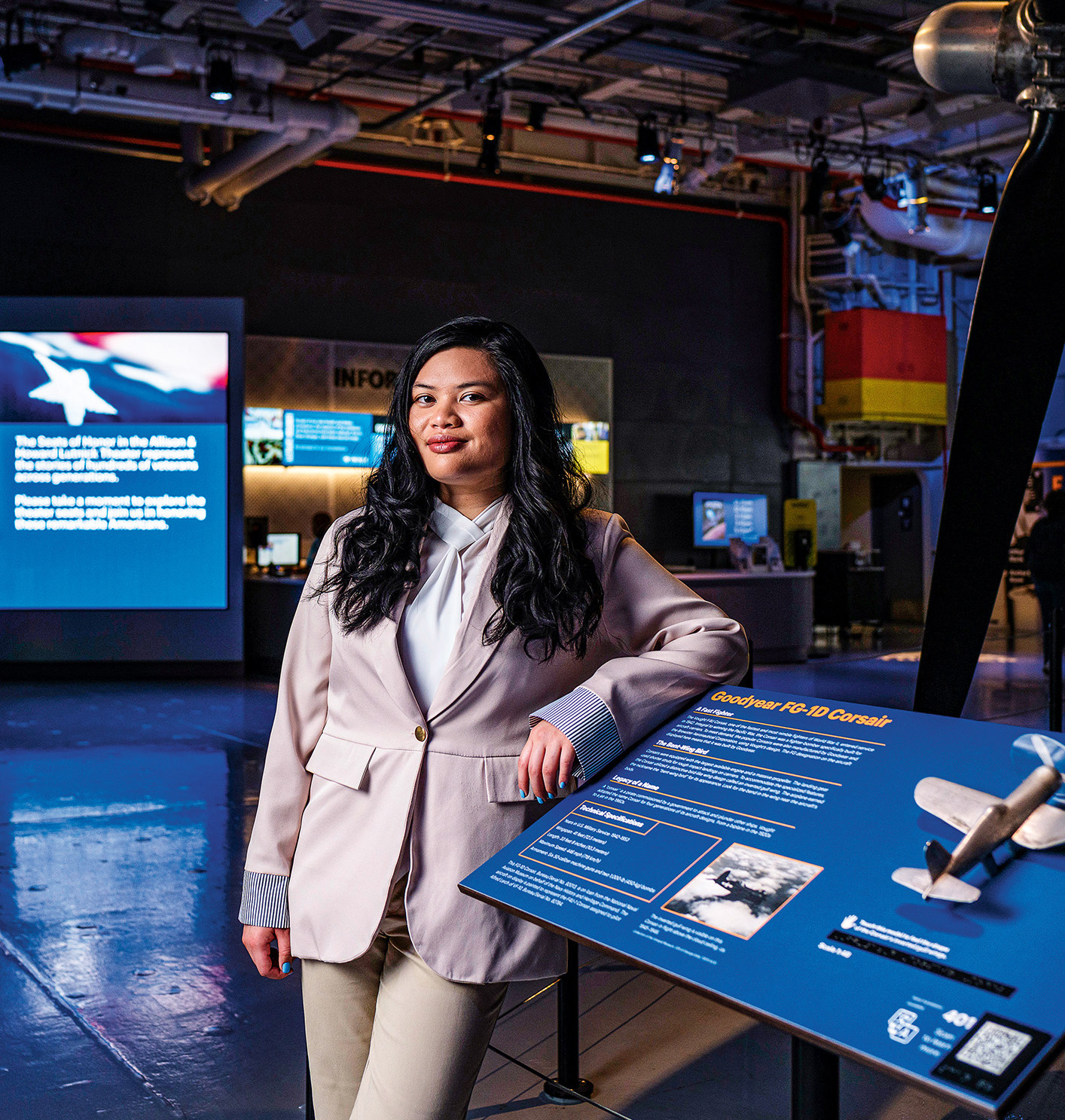 A woman wearing a suit poses for a photo in a museum.