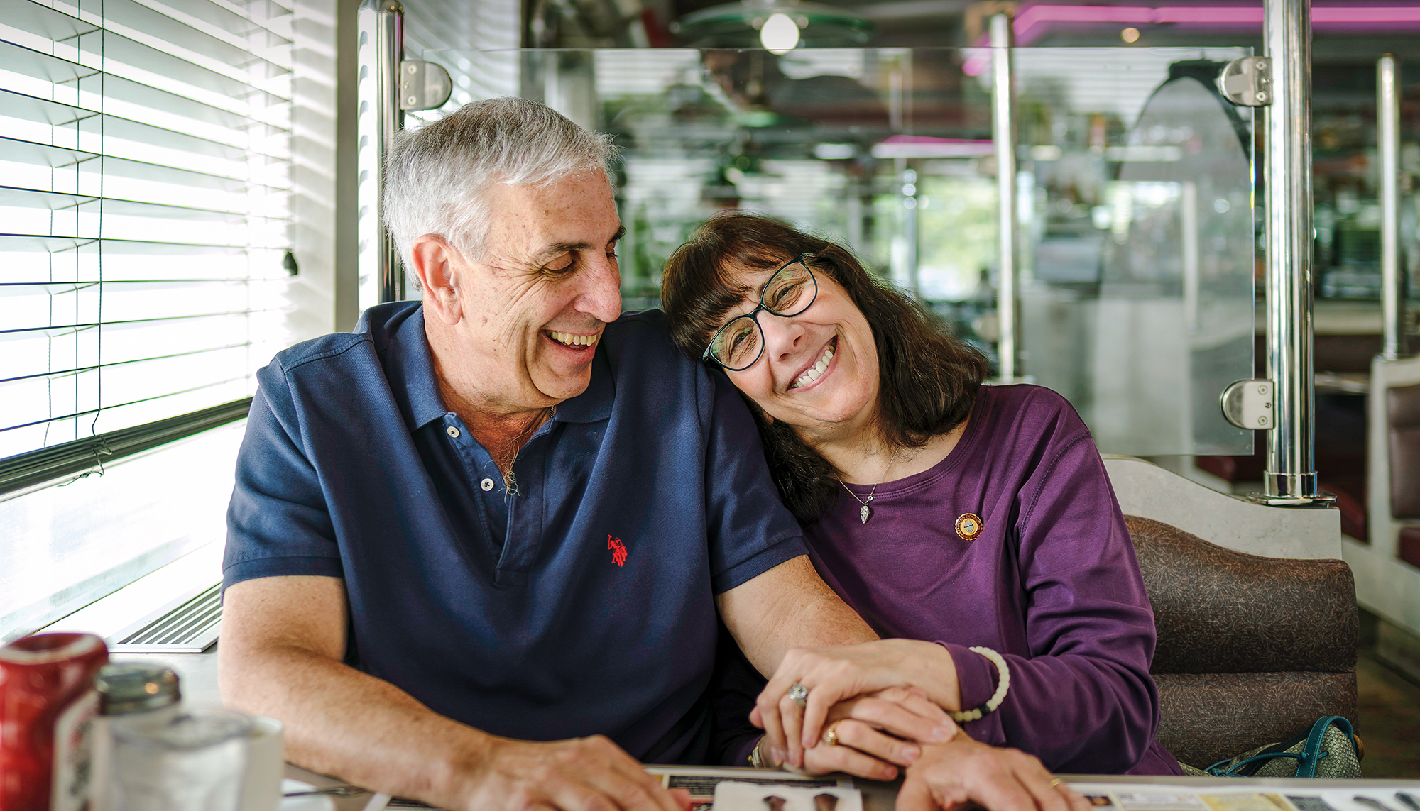 A man and a woman share a booth at a restaurant. Her head is resting on his shoulder.