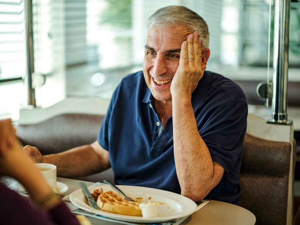 A man sits in a diner booth with a plate of waffles in front of him.