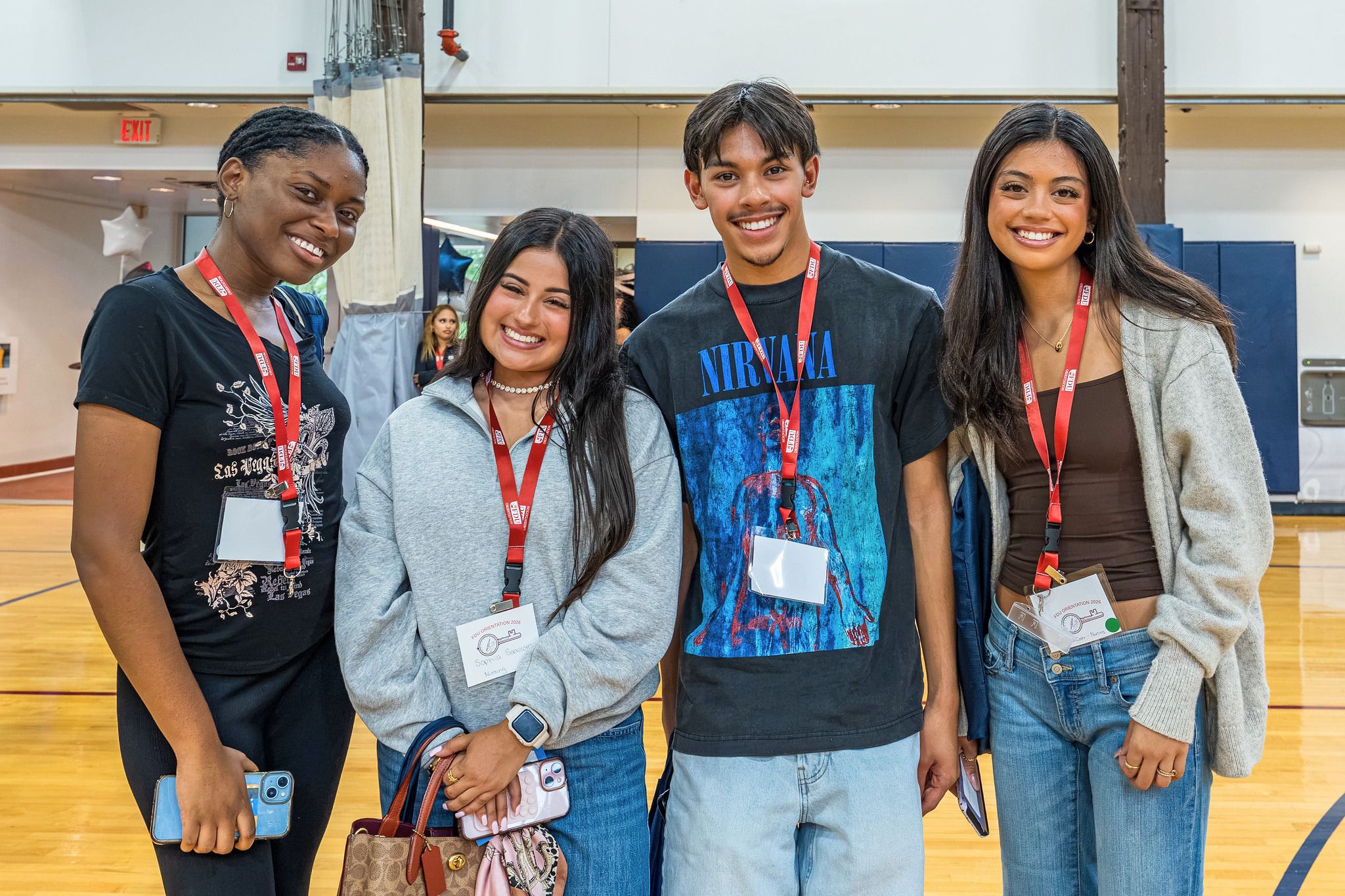four college students stand in a gymnasium and smile for the camera. they wear FDU lanyards.