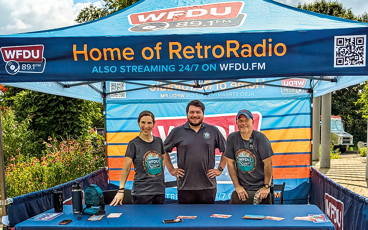 Three people stand under a WFDU tent.