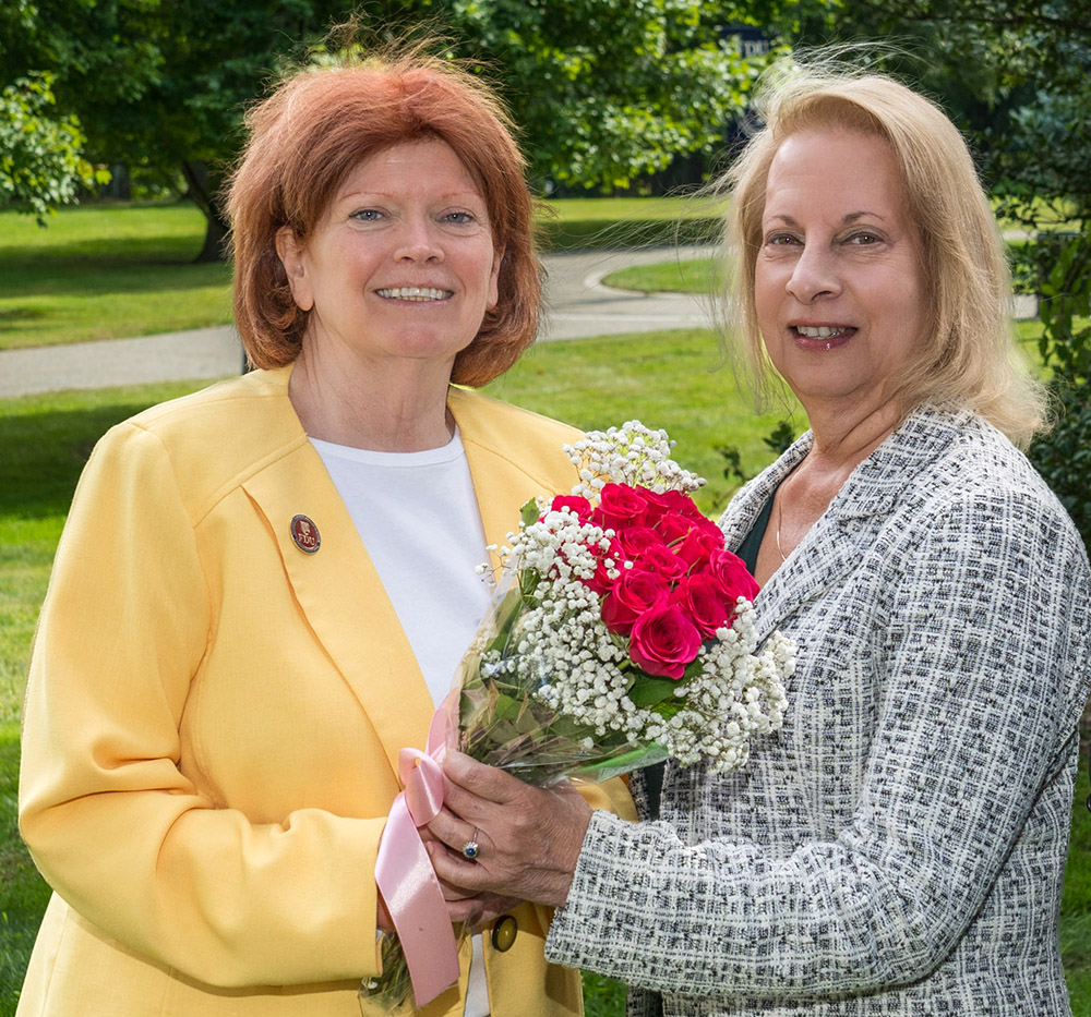 Two women hold a bouquet of flowers and smile for a photo.