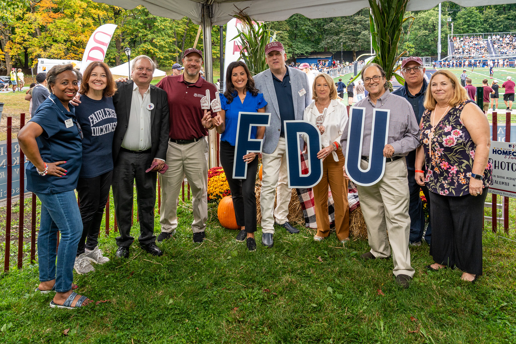 a group stands with an FDU sign and alumni merchandise. there are pumpkins next to them.