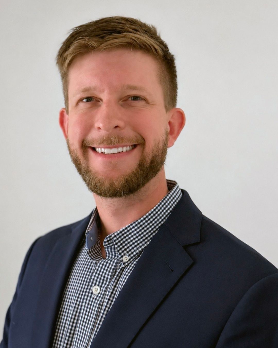a headshot of a man. he wears a dark blue blazer.