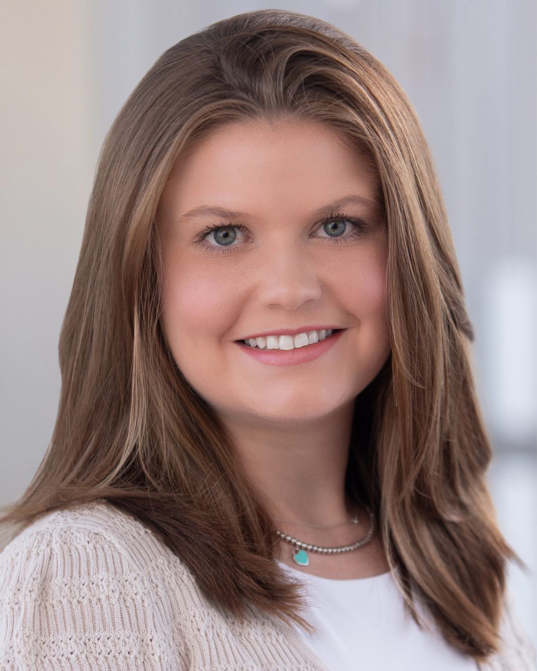 a headshot of a woman. she wears a white cardigan.