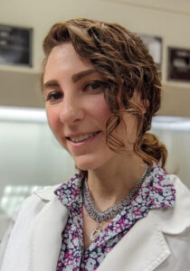 Smiling, dark haired woman in lab gown and floral blouse