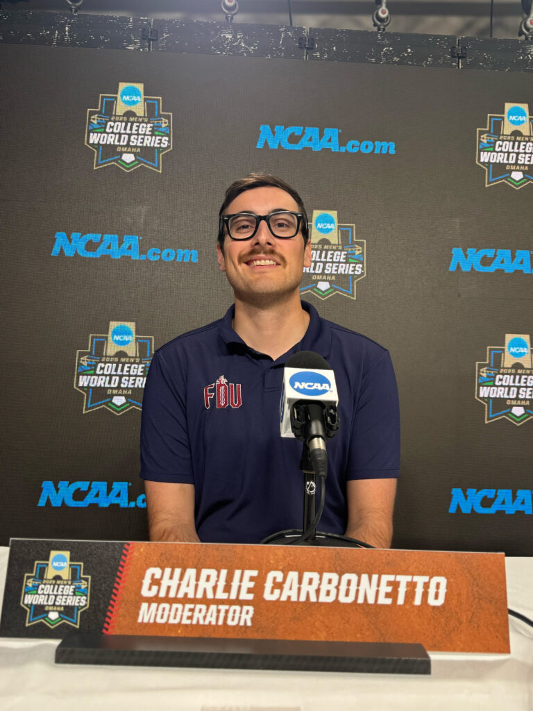 A man wearing glasses sits at a table in front of a microphone.
