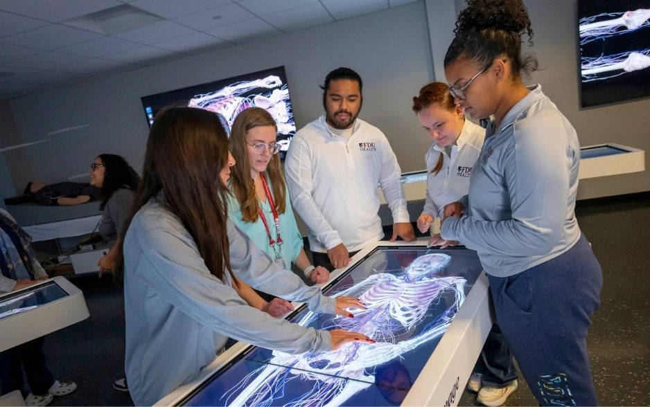 college students and a professor look down at a screen with a digital model of a human skeleton muscle system.