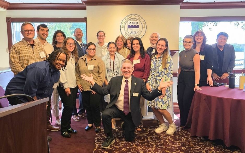 a group of college professors come together for a photo. they are dressed in business casual. one man in a suit kneels on the ground.